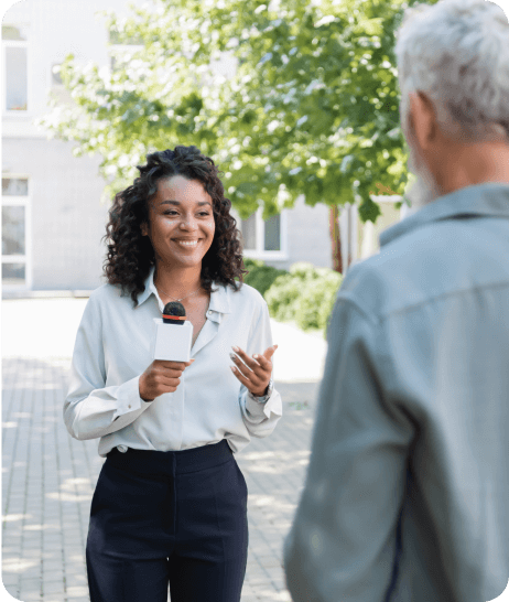 Mesa de trabalho com computador, notebook, relógio, celular e mouse, além de uma cadeira vazia