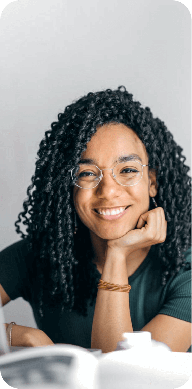 Mulher de óculos e blusa preta, sorrindo enquanto segura o queixo com uma das mãos
