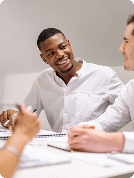 Dois homens sentados numa mesa de reunião sorrindo um para o outro